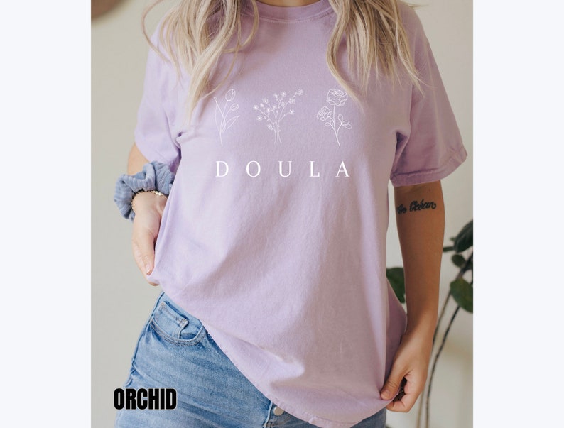 May include: A lavender t-shirt with a white graphic of three stylized flowers and the word "DOULA" printed on the front.