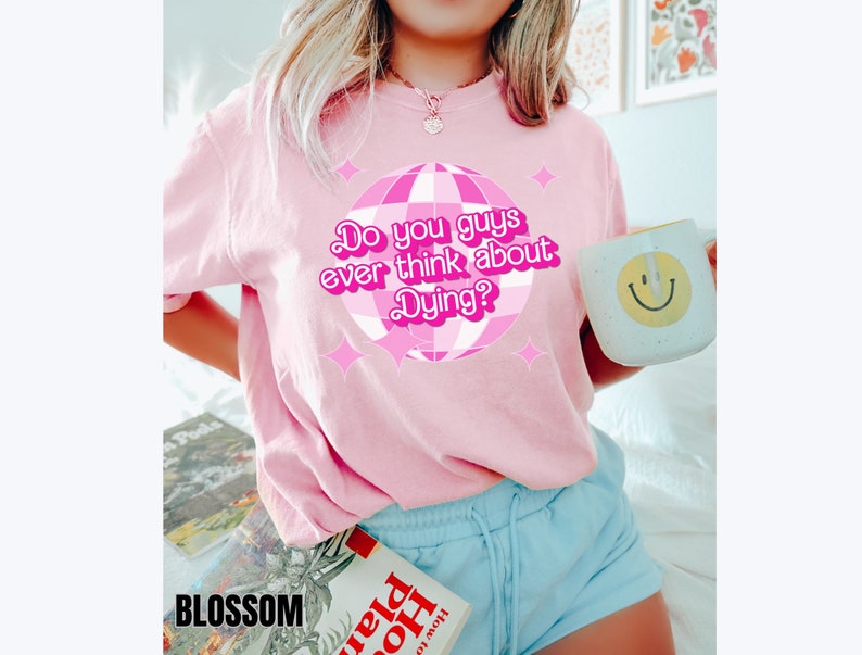 May include: Pink t-shirt with a pink disco ball graphic and the text "Do you guys ever think about Dying?"