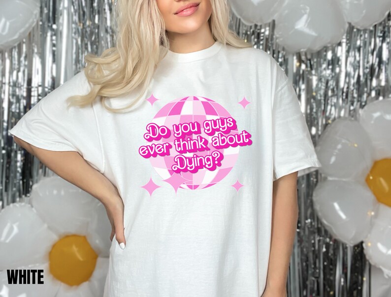 May include: White t-shirt with a pink disco ball graphic and the text "Do you guys ever think about Dying?"