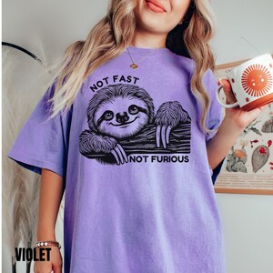 May include: Purple t-shirt with a black and white illustration of a sloth and the text "Not Fast Not Furious".
