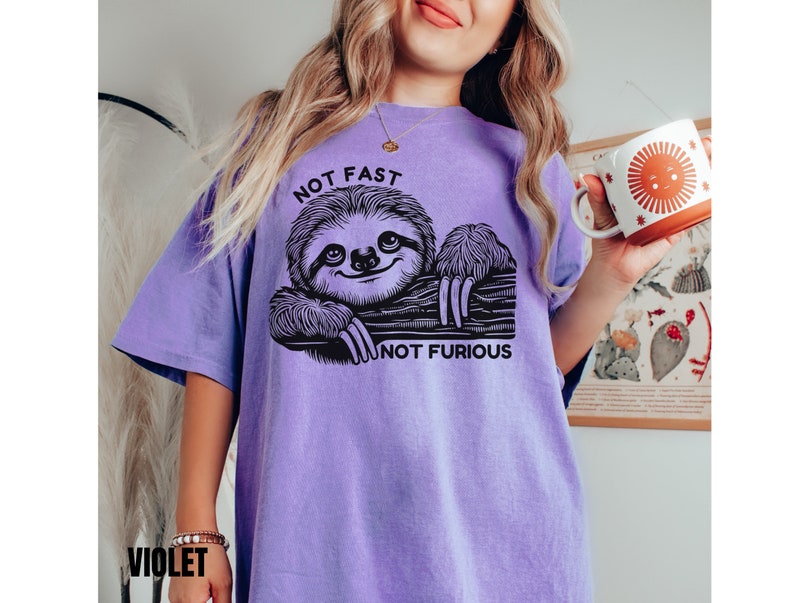 May include: Purple t-shirt with a black and white illustration of a sloth and the text "Not Fast Not Furious".