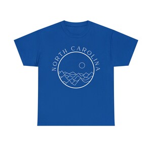 K&ouml;nnte beinhalten: K&ouml;nigsblaues T-Shirt mit einem wei&szlig;en Kreis-Motiv mit den Worten "NORTH CAROLINA" und einem stilisierten Bild von Bergen und einer Sonne.