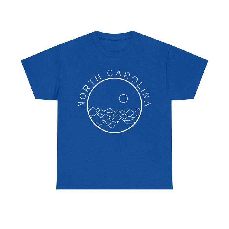 K&ouml;nnte beinhalten: K&ouml;nigsblaues T-Shirt mit einem wei&szlig;en Kreis-Motiv mit den Worten "NORTH CAROLINA" und einem stilisierten Bild von Bergen und einer Sonne.