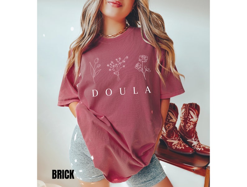 May include: A maroon t-shirt with a white graphic of flowers and the word "DOULA" printed on the front.