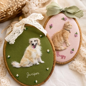 Puede incluir: Dos bastidores de bordado ovalados de madera con retratos de animales de fieltro. Uno tiene un fondo verde con un perro blanco y el nombre Juniper. El otro tiene un fondo rosa con un gato naranja, el nombre Buggy y un lazo de cinta verde.