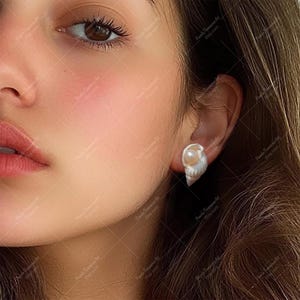 May include: A pair of shell earrings with a pearl accent. The earrings are a light brown color and have a natural shell texture. The pearl is white and round.
