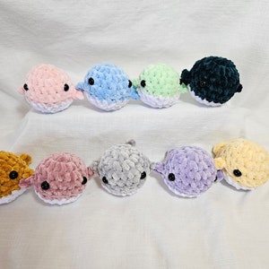 May include: A collection of ten crocheted plush pufferfish toys in various colors, including pink, blue, green, gray, purple, yellow, and brown. The toys have black eyes and white bellies.