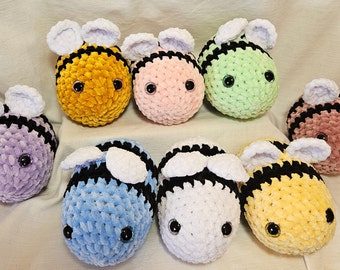 May include: Nine crocheted bee plushies in various colors, including yellow, pink, green, purple, blue, and white. Each bee has black and white stripes and white wings.