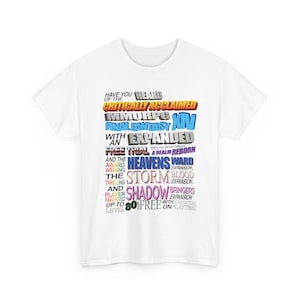 Puede incluir: Camiseta blanca con texto colorido que promociona el videojuego Final Fantasy XIV. El texto incluye frases como "Critically Acclaimed", "Heavensward" y "Shadowbringers". La camiseta tiene cuello redondo.