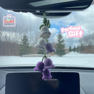 May include: Purple and white crocheted flower bells hanging from a car's rearview mirror. The flowers are arranged in a cascading design. The text "Perfect Gift" is visible in the background.