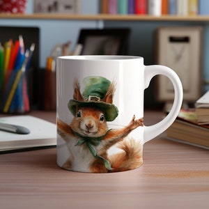 May include: White ceramic mug featuring a watercolor illustration of a squirrel wearing a green leprechaun hat and bow tie. The squirrel has its arms outstretched. The mug has a curved handle and is on a wooden surface.