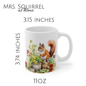 以下が含まれることがあります： 11オンスの容量を持つ白いセラミックマグカップ。マグカップには、花鉢に座っている赤いリスの水彩画が描かれています。「MRS. SQUIRREL at home」というテキストが画像の上に印刷され、「3.15 INCHES」というテキストが画像の下に印刷されています。マグカップの高さは3.74インチ、幅は3.15インチです。