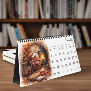 Könnte beinhalten: Ein Spiral-Schreibtischkalender für November mit einer Illustration eines Igels in einer gemütlichen Umgebung mit Kamin. Der Kalender hat einen schwarzen Ständer und steht auf einer Holzoberfläche. Im Hintergrund ein Bücherregal.