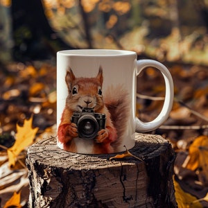 May include: White ceramic mug featuring a brown squirrel holding a camera. The squirrel is wearing a red waistcoat and has a bushy tail. The mug is resting on a tree stump with autumn leaves in the background.