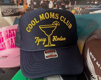 Könnte beinhalten: Ein marineblauer Trucker-Hut mit Netzrücken. Die Vorderseite des Hutes hat ein gelbes gesticktes Design mit der Aufschrift "Cool Moms Club" mit einem Margarita-Glas und den Worten "Tipsy Rodeo". Der Hut hat ein schwarz-weißes Etikett mit der Aufschrift "Otto World Famous For Front Trucker"