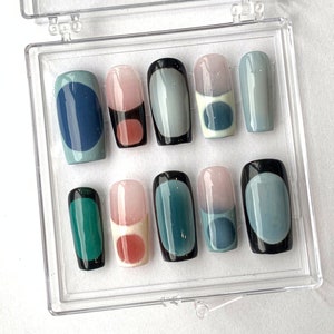 May include: A set of ten artificial nails in a clear plastic case. The nails feature a variety of designs, including solid colors, geometric shapes, and color gradients. Colors include teal, navy, pink, and black.
