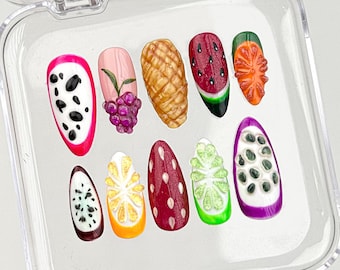 May include: A set of ten artificial nails with various fruit designs. The designs include a dragon fruit, grapes, a pineapple, a watermelon, an orange slice, and more. The nails are in a clear plastic case.