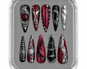 Puede incluir: Un juego de diez uñas postizas en forma de estilete en un estuche de plástico transparente. Las uñas presentan una paleta de colores rojo intenso y negro, con detalles en plata metálica, diseños en 3D, pedrería y patrones de remolinos.