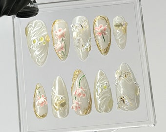 May include: Set of ten white oval-shaped false nails with gold accents and pink flower designs. Some nails have butterfly accents.