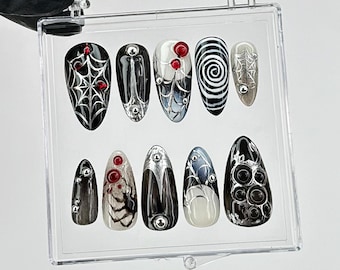 Puede incluir: Un conjunto de diez uñas postizas en una caja de plástico transparente. Las uñas presentan varios diseños, incluyendo telarañas, espirales y patrones abstractos, en negro, plata y rojo. Cada uña tiene un acabado brillante y está adornada con detalles metálicos.