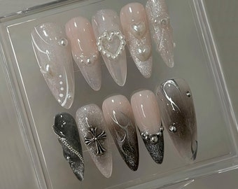 May include: A set of ten press-on nails with various designs. Some nails feature a white and silver swirl design, while others have a heart, a cross, or a swirl design with silver accents.