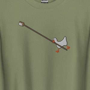 May include: A green sweatshirt with a white goose holding a stick with a marshmallow on the end. The goose is embroidered on the sweatshirt.
