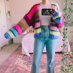 Puede incluir: Cárdigan a rayas multicolor, rosa, azul, verde y amarillo. Este tejido de punto abierto presenta mangas largas y un corte holgado. El cárdigan se lleva con vaqueros azul claro. Medidas en centímetros.