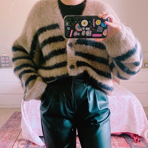 Puede incluir: Un cárdigan peludo de rayas marrones y negras con pantalones de cuero negros.