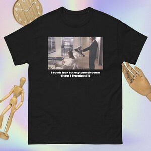 Puede incluir: Camiseta negra con una imagen impresa de una escena de película y el texto "I took her to my penthouse then I freaked it". La imagen muestra a un hombre sosteniendo una pistola de clavos.