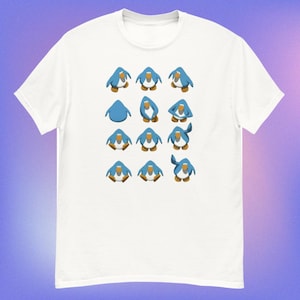 Op de afbeelding: Wit t-shirt met een patroon van blauwe pinguïns in verschillende poses. De pinguïns hebben witte buiken, oranje snavels en voeten, tegen een witte achtergrond. Het shirt is gemaakt van een zacht, comfortabel materiaal.