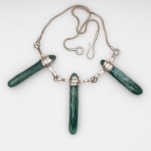 May include: A silver necklace featuring three long, green jade stones. The stones are set in silver and the necklace has a silver chain.