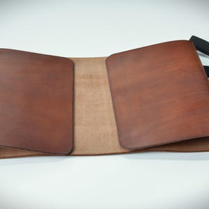 Puede incluir: Una funda de diario de cuero marr&oacute;n con una banda el&aacute;stica negra. La funda est&aacute; abierta, revelando un interior marr&oacute;n m&aacute;s claro. El cuero tiene un tono rico y c&aacute;lido, y los bordes son redondeados. La funda est&aacute; dise&ntilde;ada para un cuaderno.