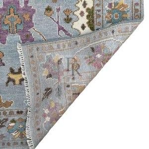 K&ouml;nnte beinhalten: Nahaufnahme der R&uuml;ckseite eines blauen und wei&szlig;en gemusterten Teppichs mit Fransen. Der Teppich hat einen hellblauen Hintergrund mit einem floralen Muster in den Farben Lila, Braun und Wei&szlig;.