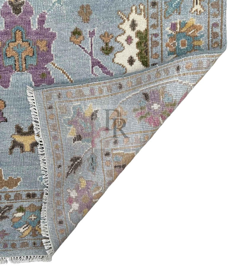 K&ouml;nnte beinhalten: Nahaufnahme der R&uuml;ckseite eines blauen und wei&szlig;en gemusterten Teppichs mit Fransen. Der Teppich hat einen hellblauen Hintergrund mit einem floralen Muster in den Farben Lila, Braun und Wei&szlig;.