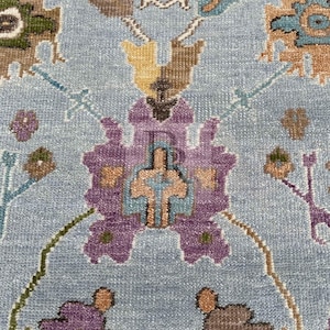 K&ouml;nnte beinhalten: Nahaufnahme eines blauen Teppichs mit Blumenmuster. Der Teppich zeigt eine Vielzahl von Farben, darunter Lila, Braun, Gelb und Gr&uuml;n. Das Muster ist kompliziert und detailliert, und der Teppich hat eine weiche, pl&uuml;schige Textur.