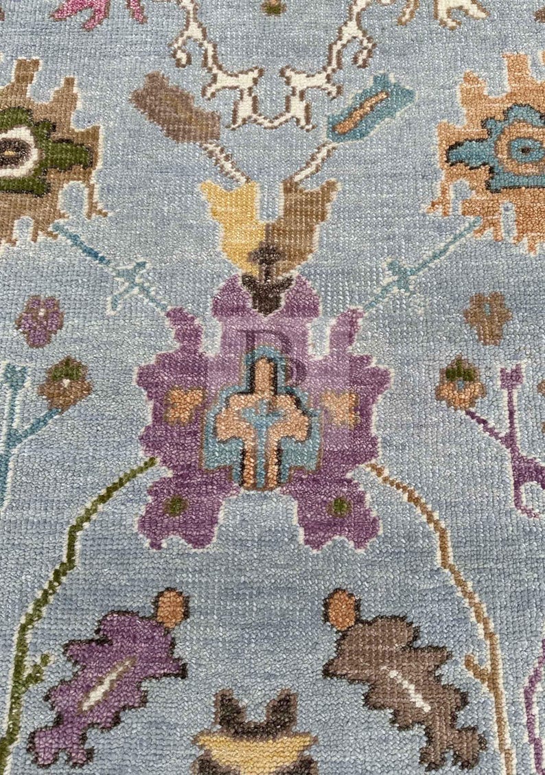 K&ouml;nnte beinhalten: Nahaufnahme eines blauen Teppichs mit Blumenmuster. Der Teppich zeigt eine Vielzahl von Farben, darunter Lila, Braun, Gelb und Gr&uuml;n. Das Muster ist kompliziert und detailliert, und der Teppich hat eine weiche, pl&uuml;schige Textur.