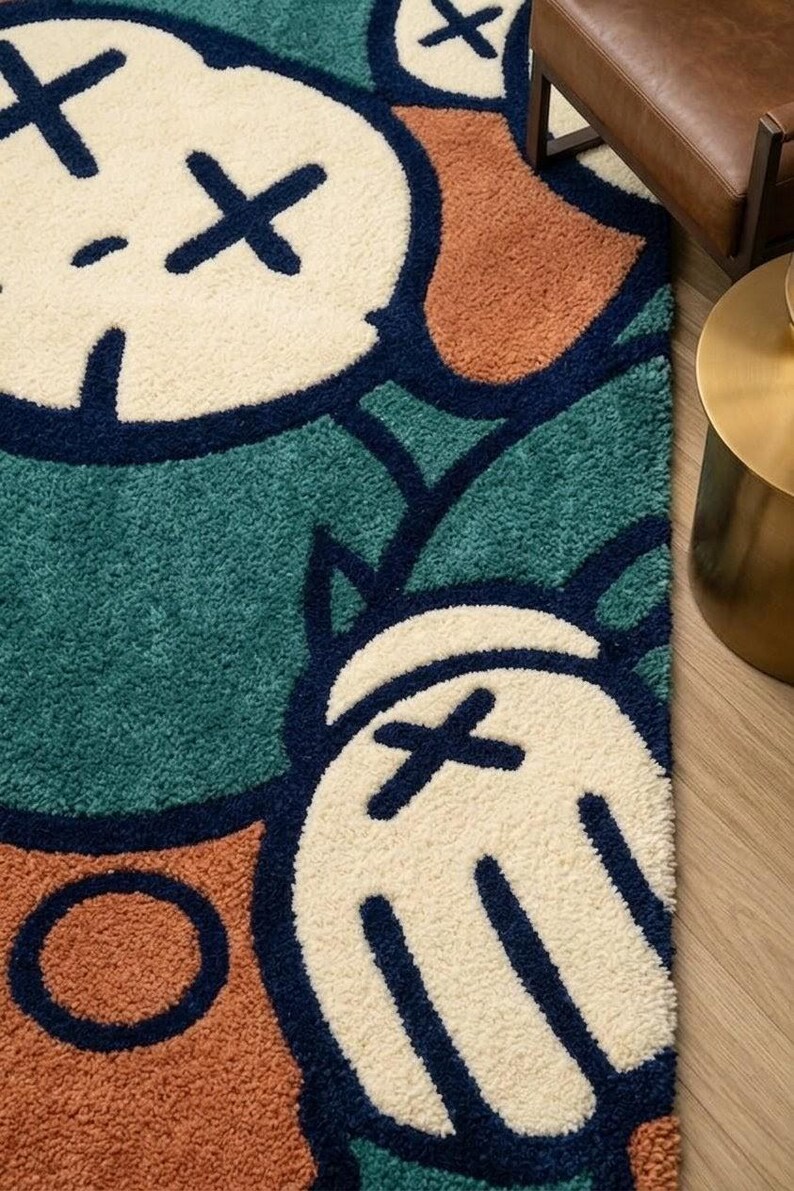 K&ouml;nnte beinhalten: Nahaufnahme eines farbenfrohen Teppichs mit einem Cartoon-Charakter-Design. Der Teppich hat einen t&uuml;rkisgr&uuml;nen Hintergrund mit cremefarbenen Formen und orangefarbenen und marineblauen Akzenten. Der Teppich besteht aus einem weichen, strukturierten Material.