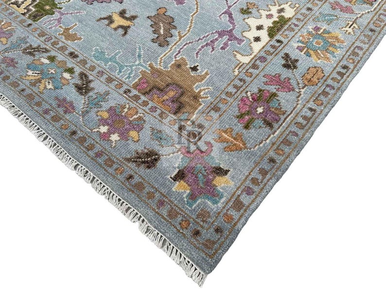 K&ouml;nnte beinhalten: Nahaufnahme eines blauen Teppichs mit Fransenrand. Der Teppich hat ein florales Muster in den Farben Rosa, Lila, Braun und Gelb.