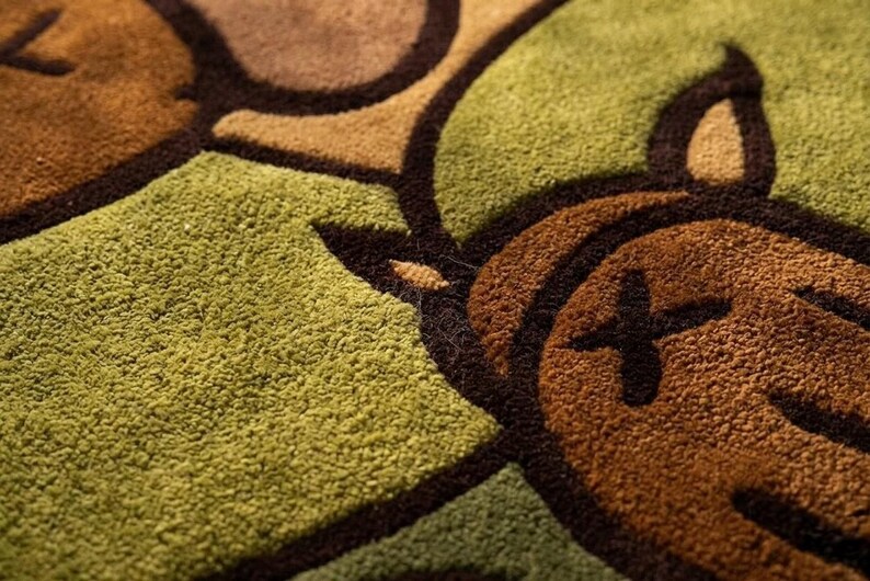 Pode incluir: Close-up de um tapete texturizado com um padr&atilde;o repetitivo em tons de castanho e verde. O design apresenta formas arredondadas com contornos castanhos escuros e um detalhe em forma de cruz.