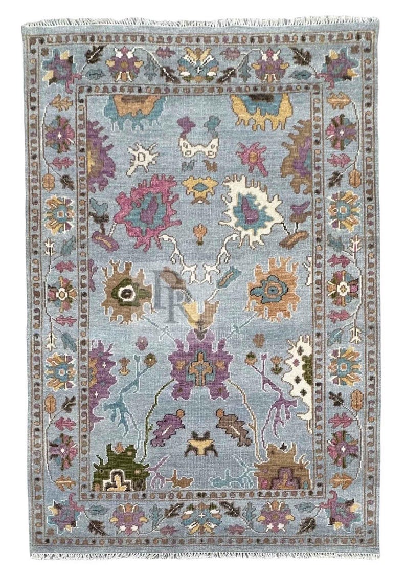 K&ouml;nnte beinhalten: Ein blauer Teppich mit einem floralen Muster in den Farben Rosa, Lila, Braun und Gr&uuml;n. Der Teppich hat einen Fransenrand.