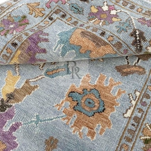 Luxury hand-knotted New Zealand wool rug with blue, gold, and purple abstract Oushak pattern. Detailed close-up of artisan craftsmanship and plush texture for high-end interior design.