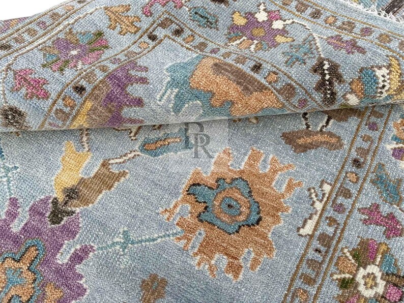 Luxury hand-knotted New Zealand wool rug with blue, gold, and purple abstract Oushak pattern. Detailed close-up of artisan craftsmanship and plush texture for high-end interior design.