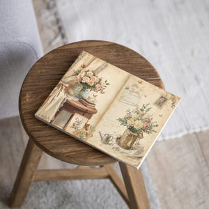 K&ouml;nnte beinhalten: Eine dekorative Keramikfliese mit einem Vintage-Blumenmuster. Die Fliese zeigt Str&auml;u&szlig;e aus Rosen und anderen Blumen in Vasen und K&ouml;rben, mit einer weichen, ged&auml;mpften Farbpalette. Die Fliese liegt auf einem kleinen, runden Holzschemel.