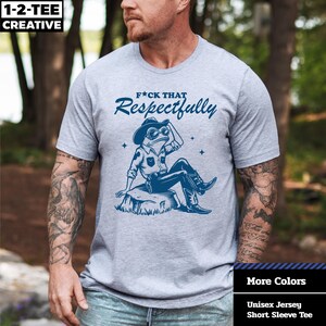 May include: A heather gray unisex short sleeve tee with the text "F*CK THAT Respectfully" above a blue illustration of a frog wearing a cowboy hat and boots. The shirt also has the text "More Colors" and "Unisex Jersey Short Sleeve Tee".