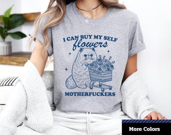 Peut inclure: T-shirt unisexe gris à manches courtes avec l'inscription "I CAN BUY MY SELF flowers MOTHERFUCKERS" et un dessin de chat avec un chariot de fleurs. Le t-shirt porte également l'inscription "More Colors" et "Unisex Jersey Short Sleeve Tee".