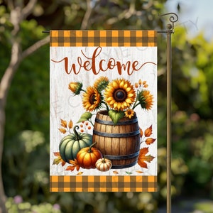May include: A welcome sign with a white wooden background and a checkered orange and brown border. The sign features a painted welcome message, a barrel filled with sunflowers, and pumpkins.
