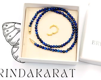 Puede incluir: Un collar de cuentas de lapislázuli azul y un pendiente de oro en una caja blanca con el texto "RIND AKARAT".