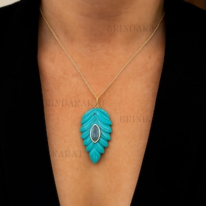 May include: A gold chain necklace with a turquoise leaf pendant. The pendant has a carved leaf design with a central oval-shaped stone. The necklace is displayed against a dark background.