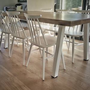 Peut inclure: Une table à manger en bois blanc avec un plateau en bois naturel et des pieds en métal blanc. La table est entourée de six chaises en bois blanc.