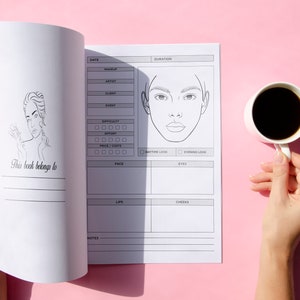May include: A white notebook with a black line drawing of a woman's face on the cover. The notebook is open to a page with a checklist for makeup looks. The text "This book belongs to" is on the cover.